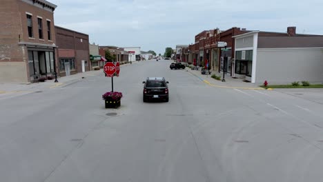 Black-Ford-Bronco-driving-downtown-State-Center,-Iowa-with-drone-video-rolling-from-behind