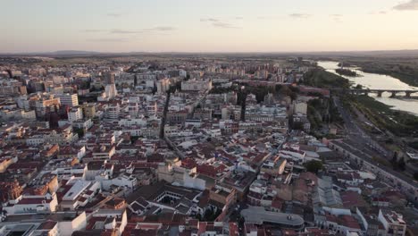 Drone-flyover-Badajoz-riverside-cityscape-during-sunset-lights,-Spain