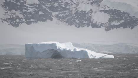Großer-Eisberg-Mit-Loch-In-Der-Mitte-Und-Küstenlinie-Im-Hintergrund