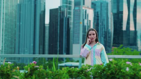 beautiful-caucasian-girl-in-a-thinking-position,-Daylight,-outside-in-chicago-with-skyscrapers-in-background-and-green-bushes-in-foregrround
