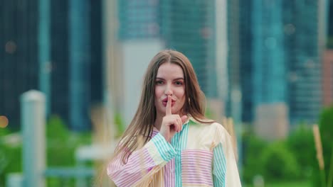caucasian-pretty-lady-looking-at-camera-makes-gesture-silence-sign-pretends-to-close-zip-up-mouth-keep-secret-information-silent-outside-with-a-corporate-feeling---chicago-skyscrapers-background