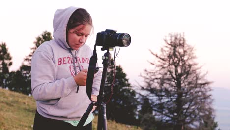 A-young-caucasian-girl-preparing-her-camera-for-timelapse-shooting,-capturing-stunning-footage-of-alpine-meadows-in-the-summer
