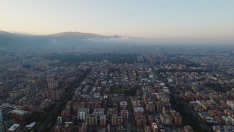 Aerial-Drone-View-Rising-Above-Large-Urban-City-Metropolitan-Area-During-Peaceful-Misty-Morning-Sunrise-With-Mountain-Background