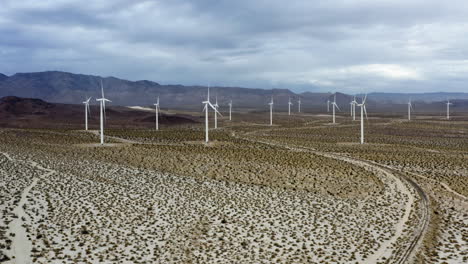 Drone-shot-approaching-a-group-of-wind-turbines,-in-the-gloomy-deserts-of-southwest-USA