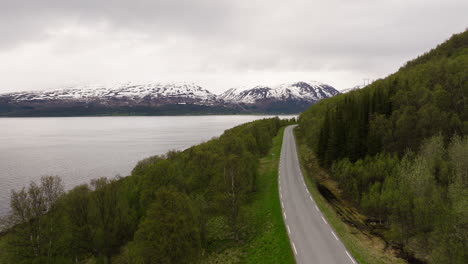 Paisaje-De-Carretera-Sinuosa-Con-Vistas-Al-Mar-Y-Los-Alpes-A-Lo-Lejos-En-Un-Día-Nublado-En-El-Norte-De-Noruega
