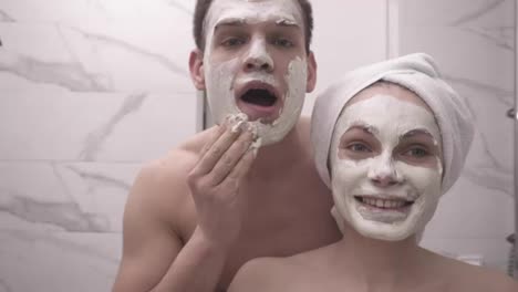 Happy-positive-young-couple-man-and-woman-having-fun-while-standing-in-a-bathroom-after-shower.-Both-playfully-applying-white
