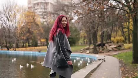 Attractive-woman-with-red-hair-walking-around-a-park-with-artificial-lake.-She-is-turning-aroung-and-smiling-to-the-camera