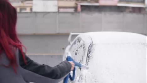 Young-woman-in-coat-applying-foam-on-her-silver-sportcar-with-special-jet-on-self-service-carwash