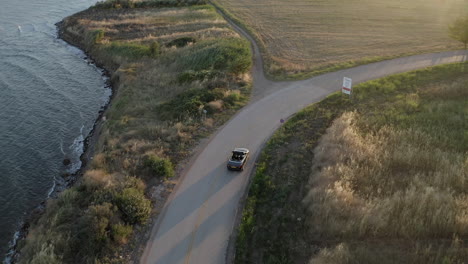 Aerial-tracks-black-convertible-in-olive-groves-on-Greek-coastal-road
