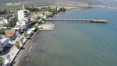 Low-waterfront-aerial-view-of-beach-patio-and-pier-on-coastal-Greece