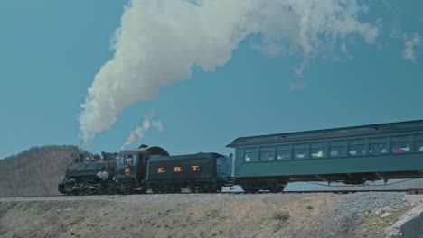 A-View-of-a-Restored-Narrow-Gauge-Steam-Passenger-Train,-Passing,-Blowing-Smoke-and-Steam-Up-a-Grade-on-a-Spring-Day