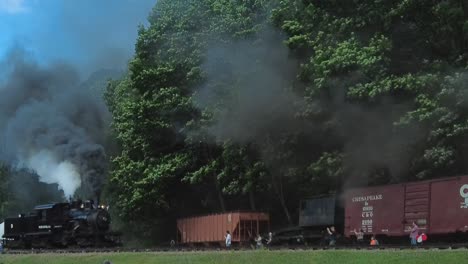 A-View-of-a-Climax-Steam-Engine-Approaching,-Blowing-Smoke-and-Steam,-Passing-Freight-Cars-on-a-Sunny-Summer-Day