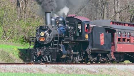 A-View-of-a-Classic-Steam-Passenger-Train-Passing,-Blowing-and-Puffing-Smoke-and-Steam-on-a-Spring-Day