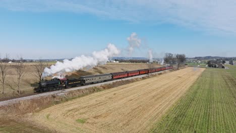 A-Drone-Slow-Motion-View-of-a-Steam-Passenger-Train,-Approaching,-Traveling-Thru-Harvested-Farmlands-on-a-Sunny-Fall-Day