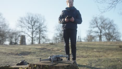Young-male-dronepilot-setting-up-a-drone-and-lift-off-into-the-air-with-remote-control-for-flying-on-a-drone-operation-in-nature-on-a-cold-spring-morning