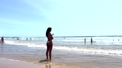 Lonely-woman-standing-on-the-beach-and-looking-at-the-sea-with-her-feet-in-the-water