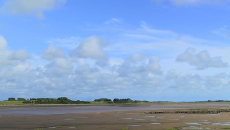 Fluffy-clouds-blowing-across-river-estuary-with-cloud-shadows,-time-lapse-60x-at-River-Wyre-estuary,-Fleetwood,-Lancashire,-England,-UK