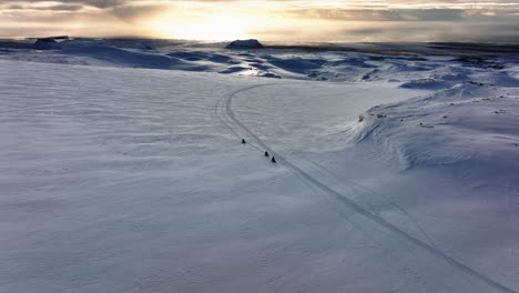 Vista-Aérea-De-Personas-Montando-Motos-De-Nieve-En-El-Glaciar-Myrdalsjokull-En-Islandia,-Durante-Una-Puesta-De-Sol-épica