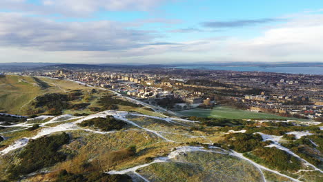 Aerial-sweeping-shot-over-a-snowy-Arthur's-seat-in-Edinburgh-on-a-crisp-winters-day