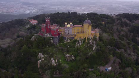 Reveal-shot-of-medieval-castle-Palácio-da-Pena-Portugal-on-cloudy-day,-aerial