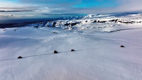 Aerial-panoramic-landscape-view-of-people-riding-snowmobiles-on-Myrdalsjokull-glacier-in-Iceland,-at-dusk