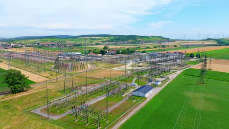 Aerial-View-Of-Electric-Substation-Industry---High-Voltage-Towers-In-Scenic-Fields---drone-shot