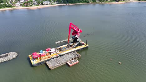 Aerial-top-down-shot-of-industrial-barge-with-mounted-crane,-Lifting-rocks-on-bay-river-during-sunny-day---Staten-Island,-New-York