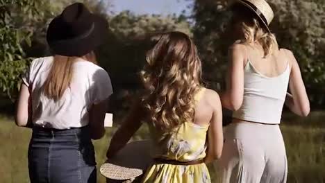 Tracking-footage-of-three-beautiful-women-in-fancy-outfit-walking-by-the-meadow-or-forest.-Sunny-day.-Picnic-outdoors