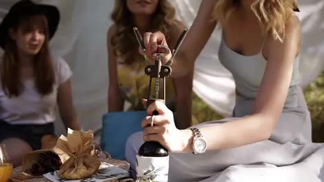 Women-on-a-picnic-with-two-her-girlfriends.-sitting-on-a-plaid.-Aim-footage-of-process-of-opening-wine-bottle.-Hen-party