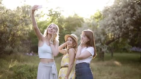 Front-view-of-three-young-women-making-selfie-with-mobile-phone,-posing.-Girls-spending-time-outdoors-in-the-garden.-Hen-party-concept