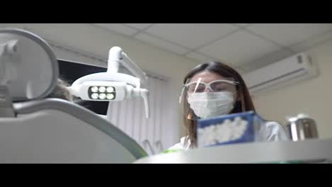 Friendly-female-dentist-turning-on-the-lights-and-taking-her-instruments-before-doing-routine-check-up-of-a-cute-little-girl.-Shot-in-4k