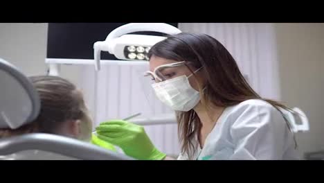 Friendly-female-dentist-examines-teeth-of-a-cute-little-girl-using-her-instruments.-Shot-in-4k