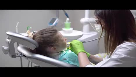 Female-dentist-drilling-tooth-of-cute-little-girl-at-the-dentist-cabinet-and-uses-saliva-ejector.-Shot-in-4k