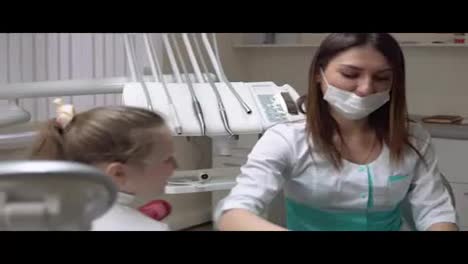 Friendly-female-dentist-taking-off-a-napking-after-procedures-and-giving-cute-little-girl-a-beautiful-green-apple.-Shot-in-4k