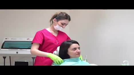 Friendly-female-dentist-putting-on-a-napking-on-young-patient.-Woman-in-dentist's-chair-preparing-to-check-up.-Shot-in-4k
