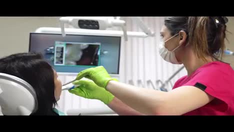 Young-female-dentist-examining-the-mouth-of-a-patient-with-an-intraoral-camera-and-showing-image-on-the-screen.-Shot-in-4k