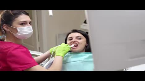 Young-female-dentist-examining-the-mouth-of-a-patient-with-an-intraoral-camera-and-showing-image-on-the-screen-explaining-to-the-patient-the-result-of-the-examination.-Shot-in-4k