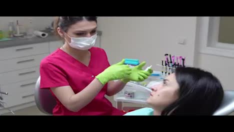 A-masked-and-gloved-dentist-explains-the-upcoming-treatment-to-his-female-patient-preparing-to-the-examination.-Shot-in-4k