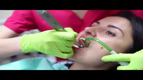 Dentist-cleans-woman's-teeth-with-professional-toothpaste-and-automatic-brush.-Dentist-using-saliva-ejector-or-dental-pump-to-evacuate-saliva.