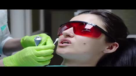 Vista-Más-Cercana-De-Las-Manos-Del-Dentista-Que-Reciben-Un-Tratamiento-Protector-Especial-En-Los-Labios-De-Una-Paciente-Antes-De-Colocar-El-Dique-De-Goma.-Filmado-En-4k