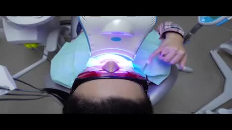 Junge-Frau-Mit-Einem-Expander-Im-Mund-Und-Roter-Schutzbrille-Lässt-Sich-In-Der-Zahnarztpraxis-Mit-Einem-UV-Gerät-UV-aufhellen.
