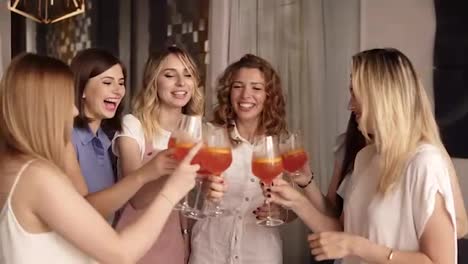 Six-beautiful-stylish-women-in-elegant-casual-outfit-celebrating-and-drinking-alcohol-cocktails.-Cheers.-Beautiful,-modern-interior.-Hen-party.-Slow-motion