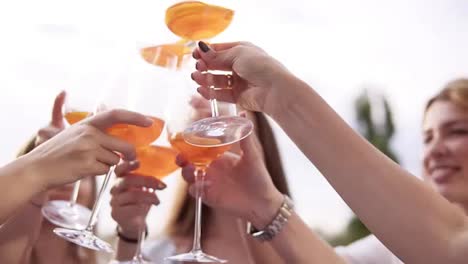 Group-of-pretty-girls-are-celebrating-and-drinking-cocktails-from-big-glasses.-Cheers.-Outdoors.-Aim-frame-of-glasses,-blurred-background.-Slow-motion