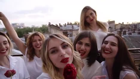 Group-of-young-women-are-hanging-out-on-a-terrace,-having-fun,-lauging.-Posing-for-camera,-taking-selfie.-All-in-a-white-with-red-lipstick.-Beautiful-old-town-view-on-a-background