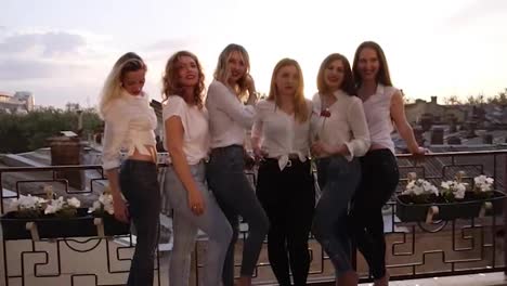 Six-caucasian-girls-are-standing-on-a-balcony-and-posing-for-the-camera.-Casual-clothes.-Close-up-of-girl's-legs-in-jeans.-Old-city-background
