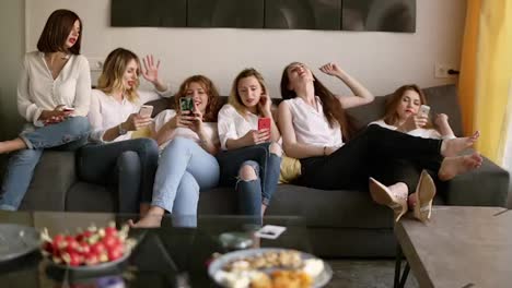 Six-beautiful-girls-relaxing-on-the-couch.-Girls-are-looking-into-their-mobile-phone.-Have-a-rest.-Hen-party-concept.-Identical-clothes.-Chatting