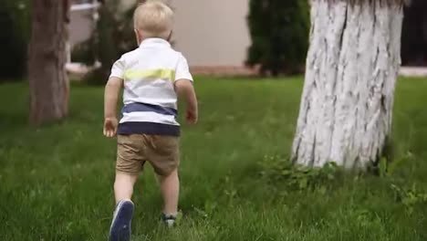 Father-and-son-play-hide-and-seek-around-tree.-Little-blonde-boy-is-running.-Happy-time.-Parenthood.-Green-grass-around