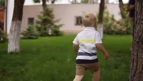 A-little-boy-is-playing-with-his-father-in-hide-and-seek-in-the-garden.-He-is-happily-running-on-the-grass.-The-father-catches-his-son,-raises-to-his-hands-and-turns-him-around.-Slow-motion