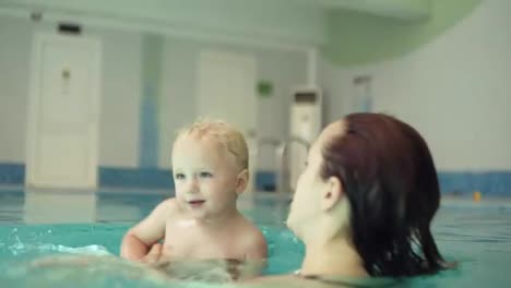 Close-up-of-a-young-wet-woman-swimming-with-his-little-blonde-son.-Whirling-above-the-water,-splashing.-Have-a-happy-time-together.-Parenthood.-Indoors-swimming-pool