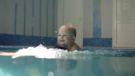 Young-man-dives-under-the-water.-Rowing-in-the-closed-swimming-pool.-Little-boy-is-onhis-fathers-back.-Smilling.-Mother-is-hugging-them.-Happy-family-time